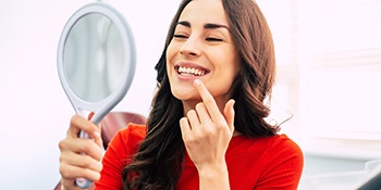 A young woman wearing a red blouse and admiring her new smile after receiving dental implants in Phillipsburg