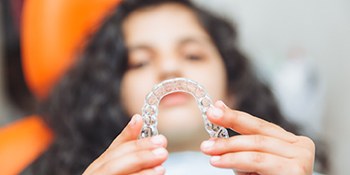 Teenage girl smiling while holding aligner in treatment chair