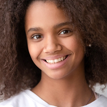 A young girl wearing a white shirt and smiling after visiting a practice that offers pediatric dentistry in Phillipsburg