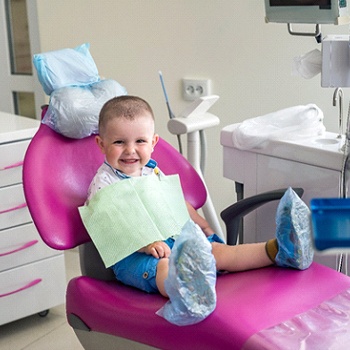 A little boy wearing covers for his shoes and sitting upright in the dentist’s chair
