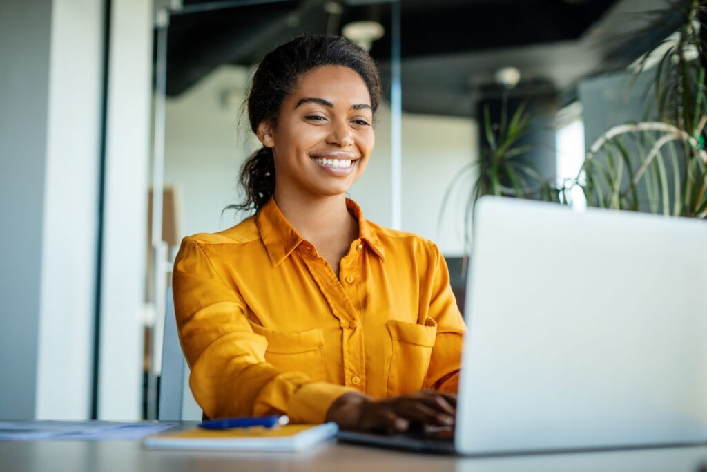 A woman in a yellow shirt smiling as she looks at a computer.