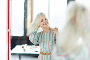 Mature woman looking at herself in a mirror and smiling brightly